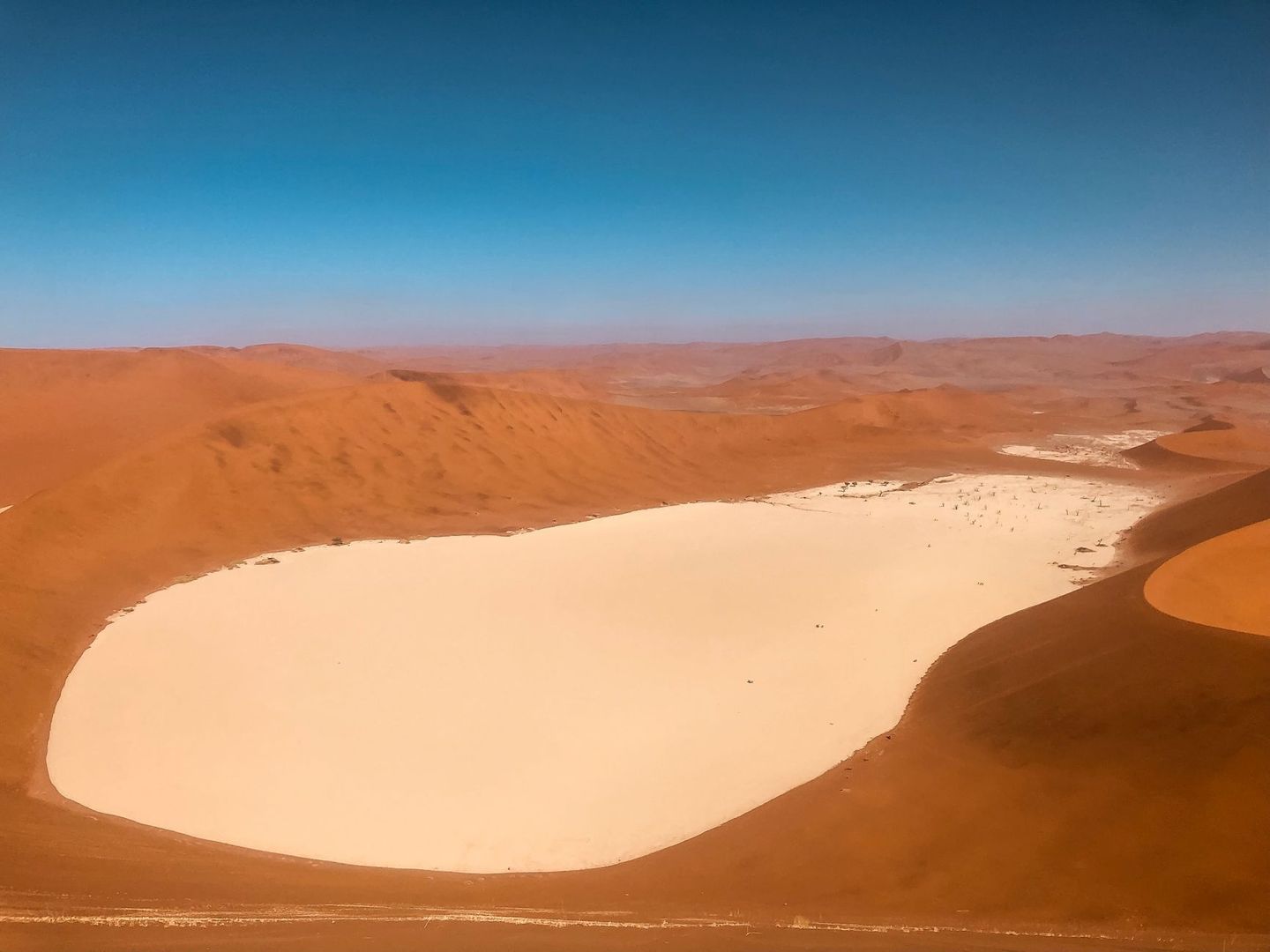 Pale clay pan surrounded by reddish desert dunes under a blue sky